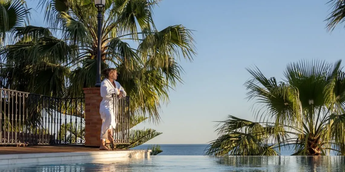 vrouw in badjas bij zwembad met palmbomen